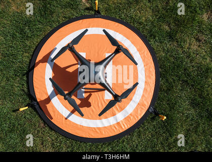 Vue de dessus d'un noir DJI Phantom 4 Obsidienne drone quadcopter Pro sur une plate-forme d'atterrissage orange entouré d'herbe sur une journée ensoleillée Banque D'Images
