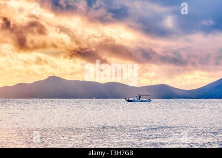 Bateau de pêche chalutier naviguant sur la mer sous un ciel nuageux spectaculaires au coucher du soleil Banque D'Images