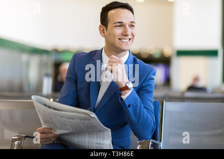 Handsome businessman professionnel lire un journal et de repos tout en restant assis dans la salle d'embarquement Banque D'Images