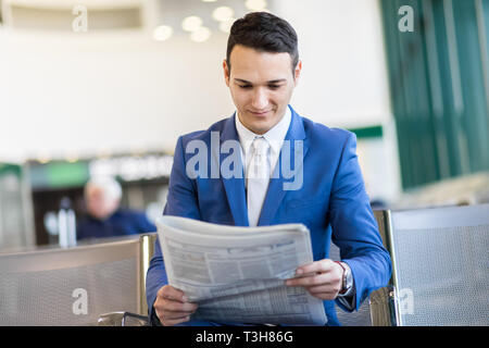 Handsome businessman professionnel lire un journal et de repos tout en restant assis dans la salle d'embarquement Banque D'Images