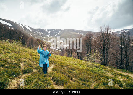 Happy smiling senior voyageur belle femme en bleu veste de pluie et un jean dans les montagnes, entourée de forêt, profiter du silence et l'harmonie de la nature Banque D'Images