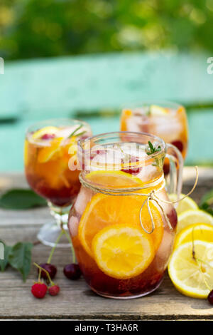Des boissons rafraîchissantes. Wine sangria ou punch aux fruits dans les verres, des cocktails de fruits frais, de baies et de romarin sur une table rustique en bois. C Banque D'Images