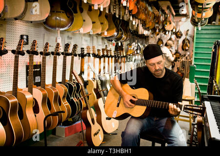 Homme strum une guitare acoustique dans un magasin de musique. Banque D'Images