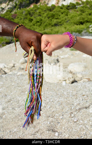 Mains de différentes races ornés de bracelets africains traditionnels, rendant fist fist pour accord et tas de bracelets africains orientation verticale Banque D'Images