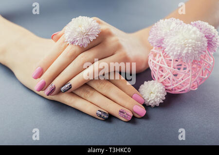 Manucure rose et noir sur les mains avec des fleurs sur fond gris. Nail art et design. Soins du corps Banque D'Images