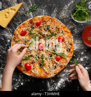 Woman decorating pizza avec salade de roquette, récolte Banque D'Images