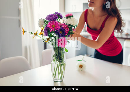 Femme met des fleurs roses dans un vase. Jeune femme au foyer en prenant soin de confort dans la cuisine. Conception de la cuisine moderne. Cuisine blanc et argent Banque D'Images