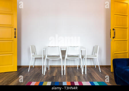 Chaises en bois blanc avec une table dans le contexte d'un mur blanc à l'intérieur avec des portes jaunes Banque D'Images