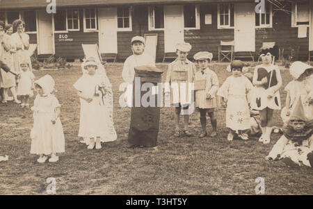 Vintage Carte postale photographique montrant un groupe d'enfants vêtus costumés dans un camp de vacances britannique Banque D'Images