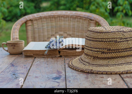 Vacances d'été concept dans le style rétro/Bouquet de fleurs de la lavande sur le vieux livre, tasse de café et vintage chapeau de paille sur la table rustique Banque D'Images