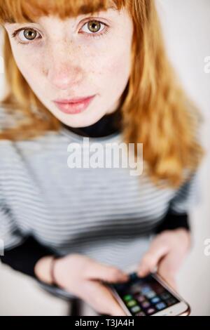 Girl, adolescent, avec le smartphone en main, regarde pensivement en appareil photo, studio shot, Allemagne Banque D'Images