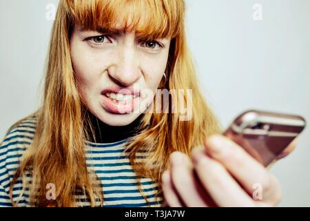 Fille, adolescent avec smartphone en main, l'air fâché, désespéré à l'appareil photo, studio shot, Allemagne Banque D'Images