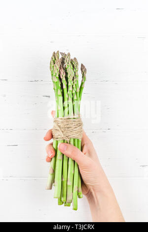 Creative style scandinave à la télévision était vue de dessus les asperges vertes fraîches dans femme les mains sur la table en bois blanc, copie d'arrière-plan de l'espace. Minimal House cooki Banque D'Images