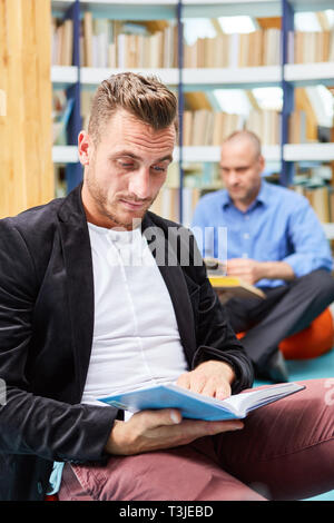 Jeune homme lit concentrées dans un livre dans la bibliothèque de la community college Banque D'Images