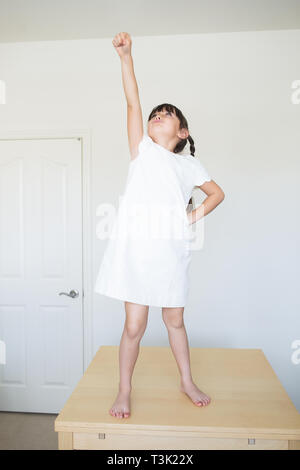 6-7 ans fille est sur le dessus de la table à la maison. Elle fait semblant de voler. Banque D'Images