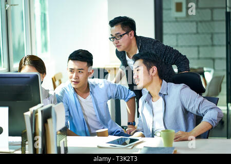 Quatre jeunes dirigeants de sociétés asiatiques travaillant ensemble discuter affaires plan à l'aide d'ordinateur de bureau en bureau. Banque D'Images