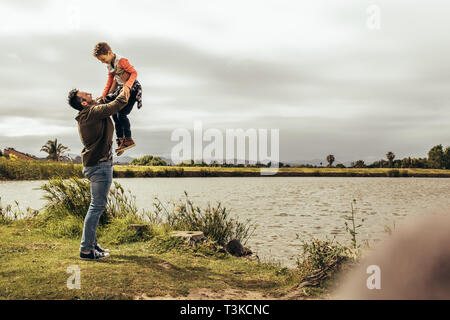 Père et fils s'amusant de passer du temps ensemble à l'extérieur. Man lifting son fils high jouer avec lui près d'un lac. Banque D'Images