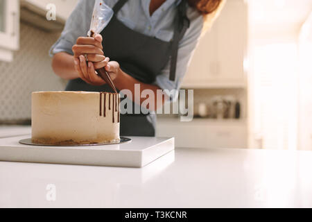 Tablier femme en décorant le gâteau avec du chocolat liquide. Chef pâtissier dans cuisine decorating cake au chocolat glaçage. Banque D'Images