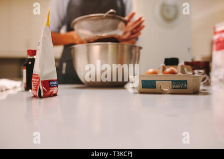 Ingrédients de cuisson sur comptoir de la cuisine avec femme sasser la farine dans le bol. Gâteau pâtissier préparation en cuisine. Banque D'Images