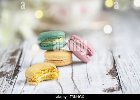 Manquant de mordre un citron macaron français devant une pile de macarons sur une table rustique blanc.. Banque D'Images