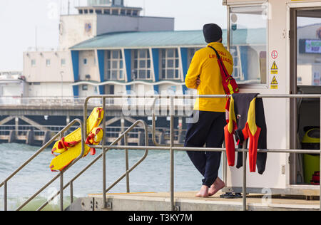 RNLI Lifeguard en service au kiosque de Lifeguard Hut avec Bournemouth Pier en arrière-plan à la plage de Bournemouth, Bournemouth, Dorset UK en avril Banque D'Images