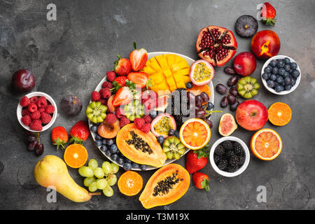 Plateau de fruits délicieux grenade mangue papaye framboises fruits de la passion oranges sur une assiette ovale de petits fruits sombres sur fond de béton, selective focus, vue du dessus, copy space Banque D'Images