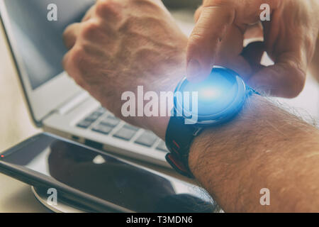 L'homme en utilisant smartwatch avec son doigt dans office, avec le smartphone et l'ordinateur portable à l'arrière-plan Banque D'Images