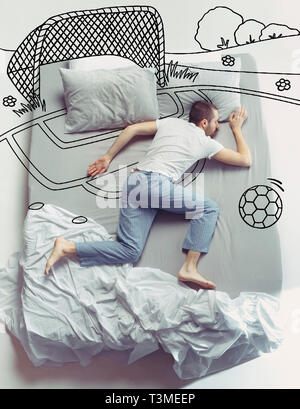 Football manquée et l'enfance. Haut Voir photo de jeune homme dormir dans un grand lit blanc à la maison. Rêves concept. À propos de rêve peint, stade, sport, activité ball, jouer, l'équipe, objectif, gagner. Banque D'Images