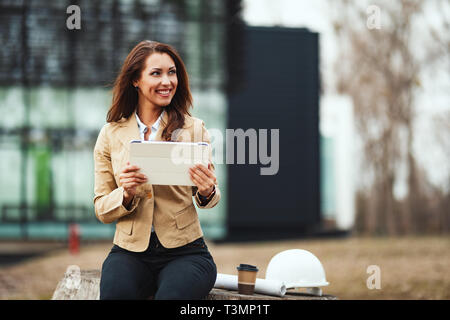 Portrait de jeune ingénieur femme avec casque blanc à côté d'elle et les bleus dans ses mains au chantier de construction. Banque D'Images