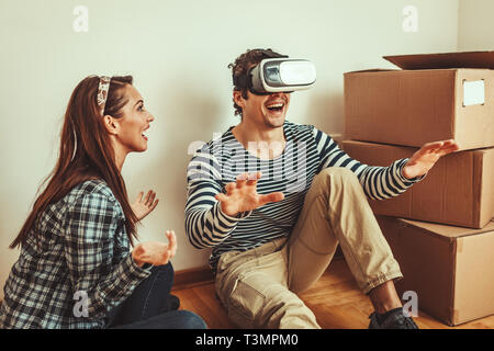 Le jeune couple est heureux de déménager dans une nouvelle maison. Ils sont unpacking boxes avec des choses dans leur nouvelle salle de séjour et d'avoir du plaisir avec la réalité virtuelle g Banque D'Images