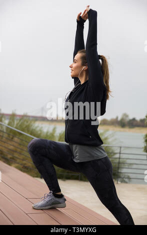 Belle jeune athlète faisant s'étendant des exercices pour les jambes à l'extérieur Banque D'Images