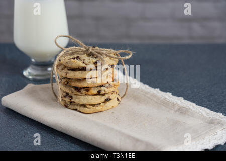 Une pile de cadeaux de cerise séchée saine cookies attachés en un arc avec de la ficelle sur une serviette ourlé de dentelle bleu assis sur un comptoir avec un verre de lait. Che Banque D'Images