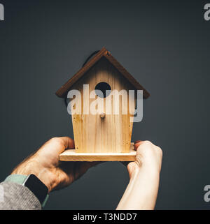 Image carrée des mâles adultes de mains tenant la nidification des oiseaux nichoir maison prête à être installée dans le jardin sur un arbre Banque D'Images