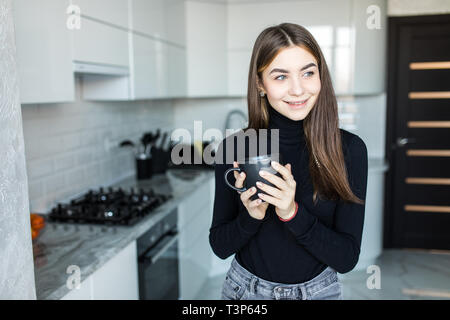 Partager vos sentiments. Cheerful nice woman smiling et boire le thé dans la cuisine Banque D'Images