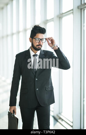 Indian businessman walking in office interior avec de grandes fenêtres avec vue sur le centre d'affaires Banque D'Images