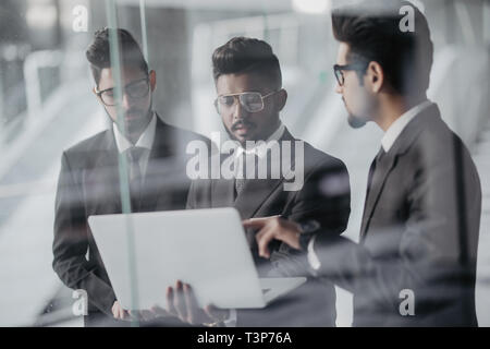 Silhouettes de trois dirigeants de sociétés asiatiques tenir devant les fenêtres discuter affaires à l'aide d'un ordinateur portable. Banque D'Images