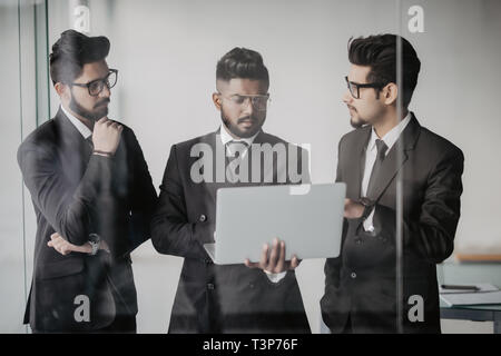 Silhouettes de trois dirigeants de sociétés asiatiques tenir devant les fenêtres discuter affaires à l'aide d'un ordinateur portable. Banque D'Images