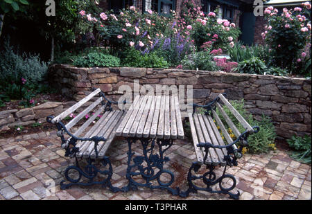 Cour-jardin en contrebas, les meubles, la brique de pavage, mur de soutènement en pierre, roses (Apple l'aube, Marie Rose & Gertrude Jekyl) Sedum, delphinium, Centranthus Banque D'Images