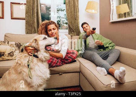 Young smiling couple hétérosexuel ensemble sur canapé avec leur chien boire d'une tasse Banque D'Images