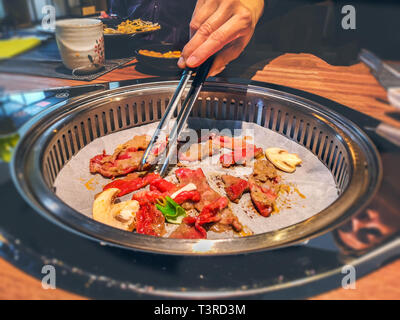 La main féminine coréenne de cuisson du boeuf bulgogi griller dans un barbecue sur table de restaurant Banque D'Images