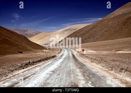 La route sinueuse qui mène à la vallée aride avec sec stérile jaune et marron des collines en désert d'Atacama, Chili Banque D'Images