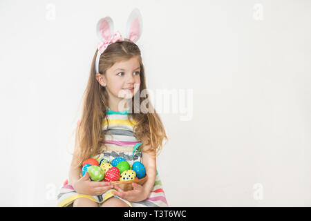 Cute little girl wearing Bunny Ears holding oeufs de Pâques peints et souriant sur un fond blanc. Banque D'Images