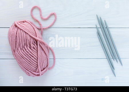 Pelote rose avec aiguilles gris blanc isolé sur fond de bois, des gants ou des bas de tricot sur 5 aiguilles à tricoter Banque D'Images