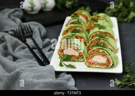 Rouleau de Lavash avec bâtonnets de crabe, les épinards, le persil, le fromage et les carottes en Korean style sur une plaque sur un fond sombre Banque D'Images