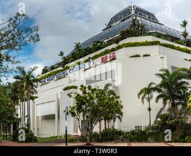 Cairns, Australie - Février 17, 2019 : blanc construction du Reef Hotel Casino sur la rue Abbott avec beaucoup de feuillage vert autour et sur le dessus. Ciel bleu Banque D'Images