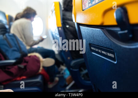 Bari, Italie - 8 mars, 2019 : Avis d'attacher la ceinture de sécurité sur le dos d'un siège d'avion. Banque D'Images
