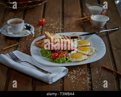 Plusieurs oeufs frits sont servis sur une assiette avec de la saucisse et salade verte avec des tomates rouges frais. Banque D'Images