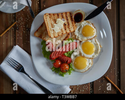 Plusieurs oeufs frits sont servis sur une assiette avec de la saucisse et salade verte avec des tomates rouges frais. Banque D'Images