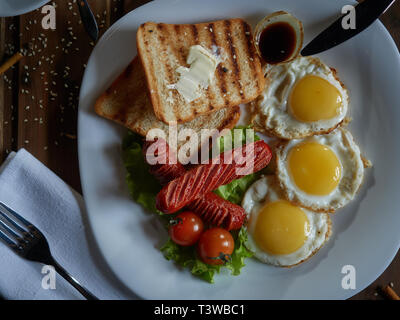 Plusieurs oeufs frits sont servis sur une assiette avec de la saucisse et salade verte avec des tomates rouges frais. Banque D'Images