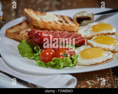 Plusieurs oeufs frits sont servis sur une assiette avec de la saucisse et salade verte avec des tomates rouges frais. Banque D'Images